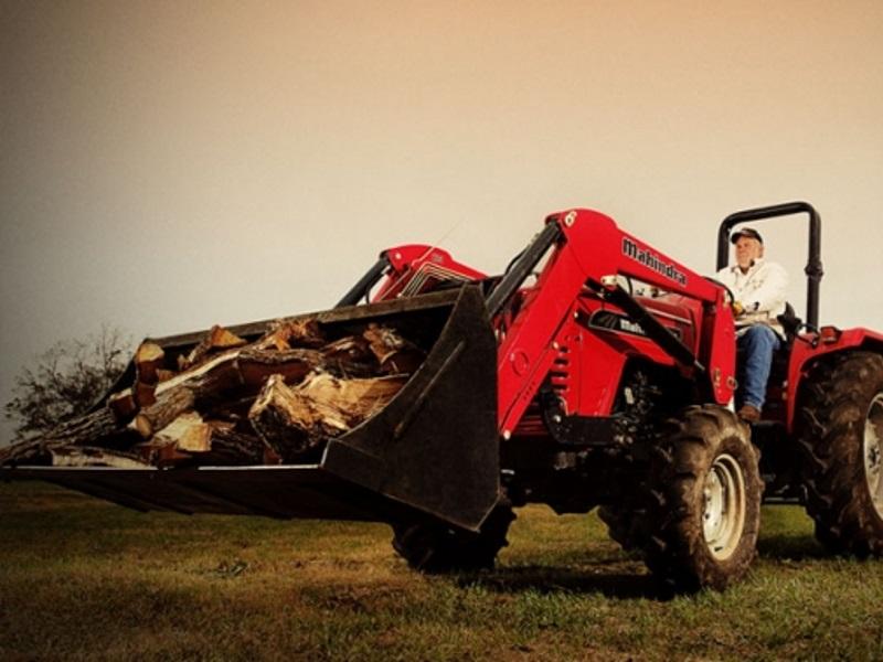 A farmer carrying debris with a red Mahindra 4540 4WD tractor.