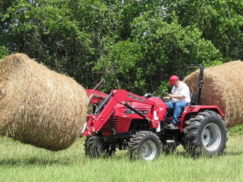 A farmer moving hay with a red Mahindra 4540 4WD Tractor.